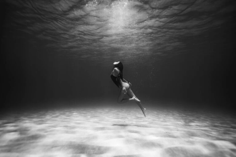 Black and White Photo of Woman Swimming Underwater