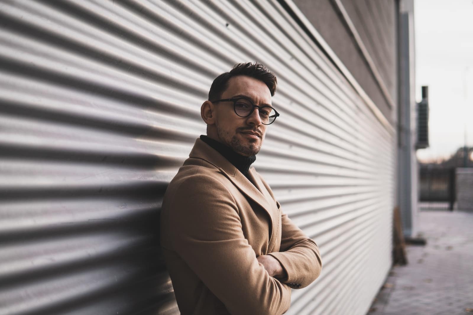 man in brown coat standing beside gray wall