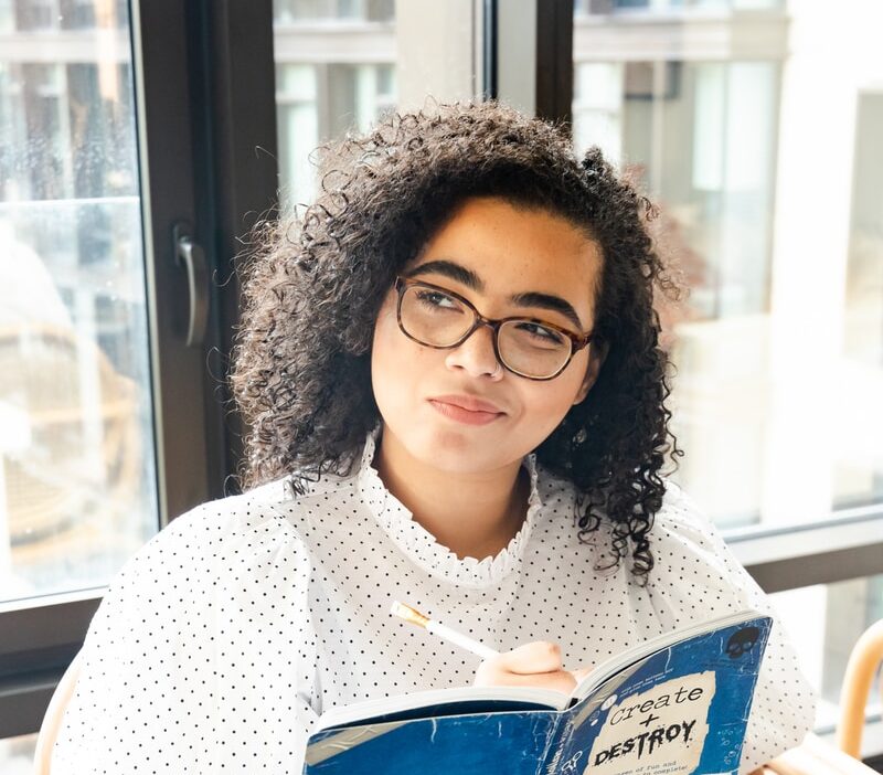 woman in white and black polka dot shirt holding blue and white book