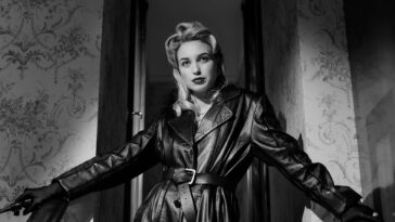 blonde woman in black leather coat standing by the stairs