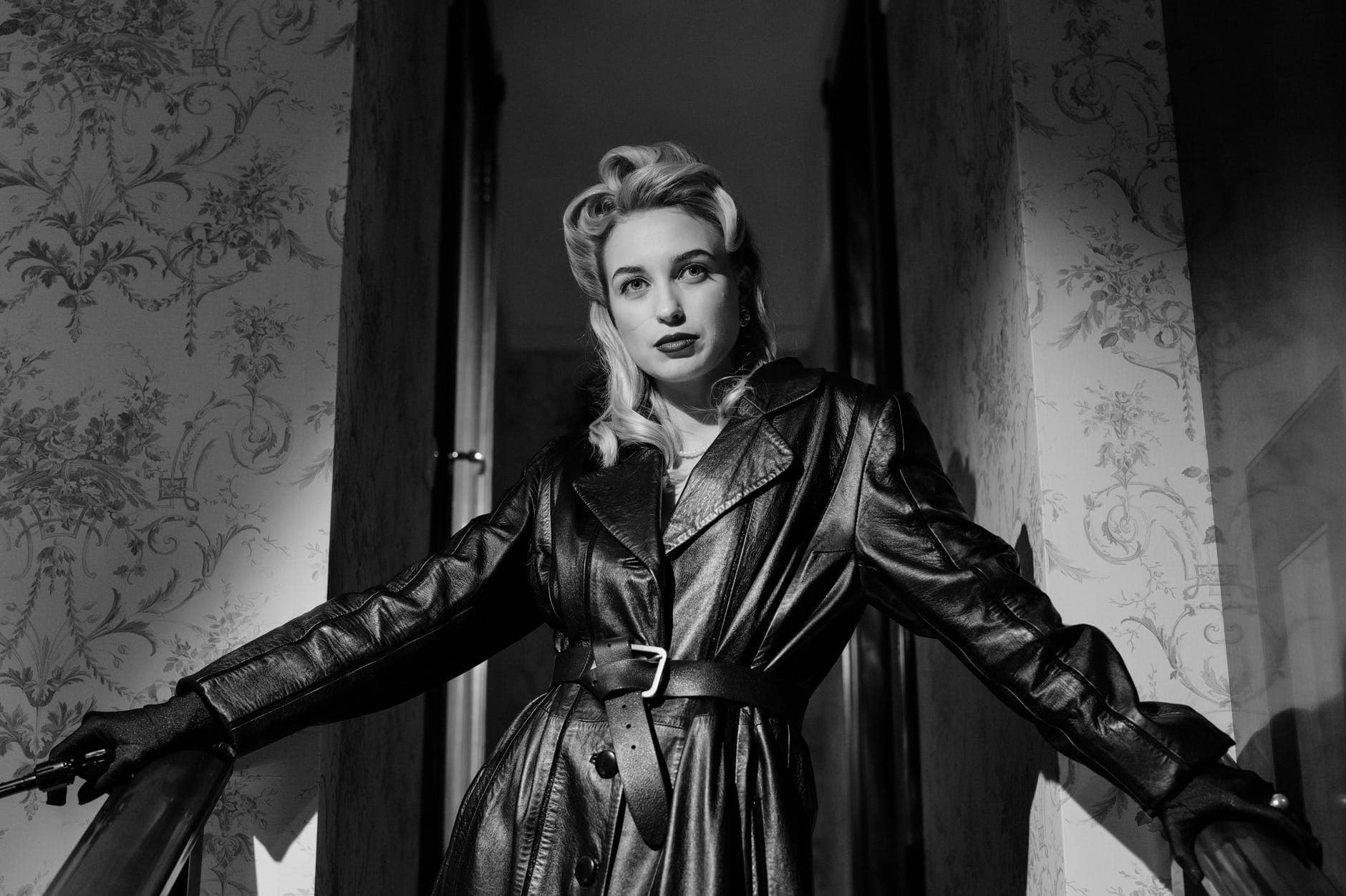 blonde woman in black leather coat standing by the stairs