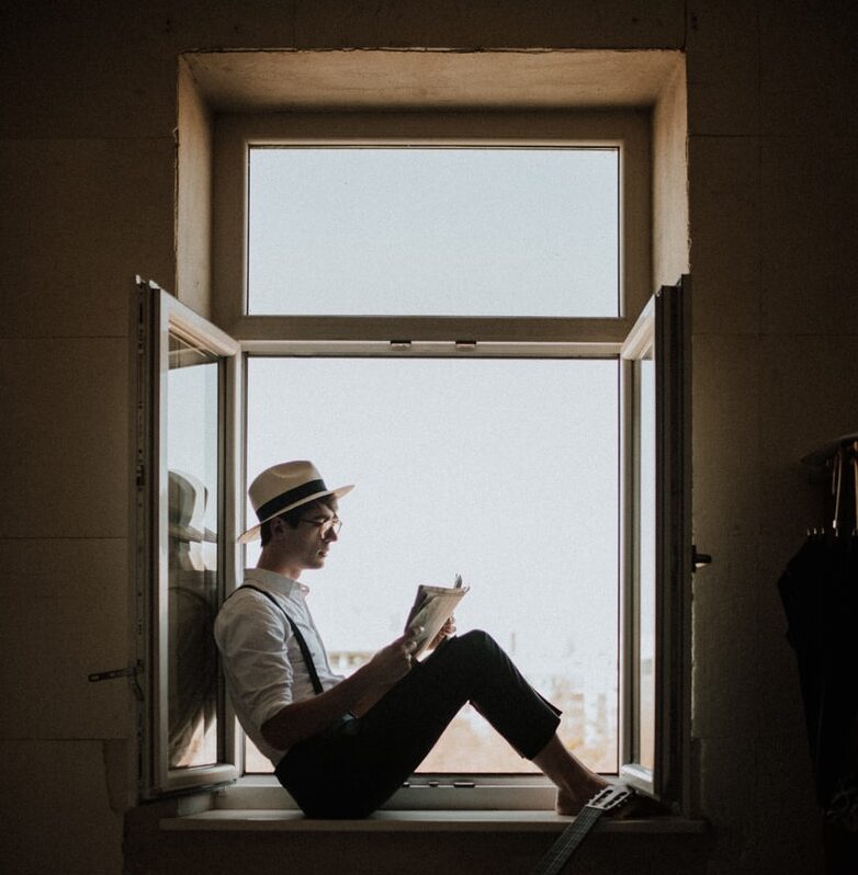 man sitting on window while reading