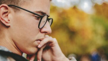 boy with black framed eyeglasses holding face