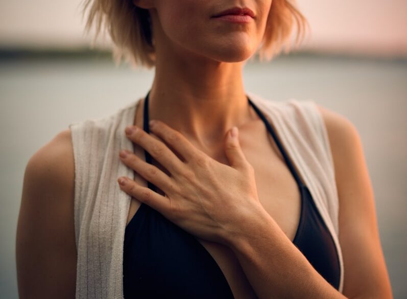 woman in white vest and black bikini with hand on chest