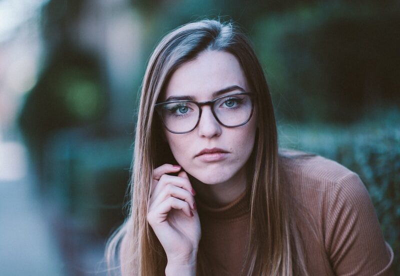 selective focus photography of woman wearing brown long-sleeved shirt and black framed eyeglasses