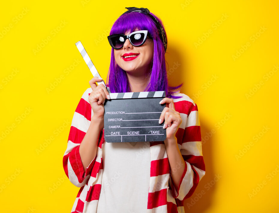 Young actres with purple hair holding a clapper on yellow background.