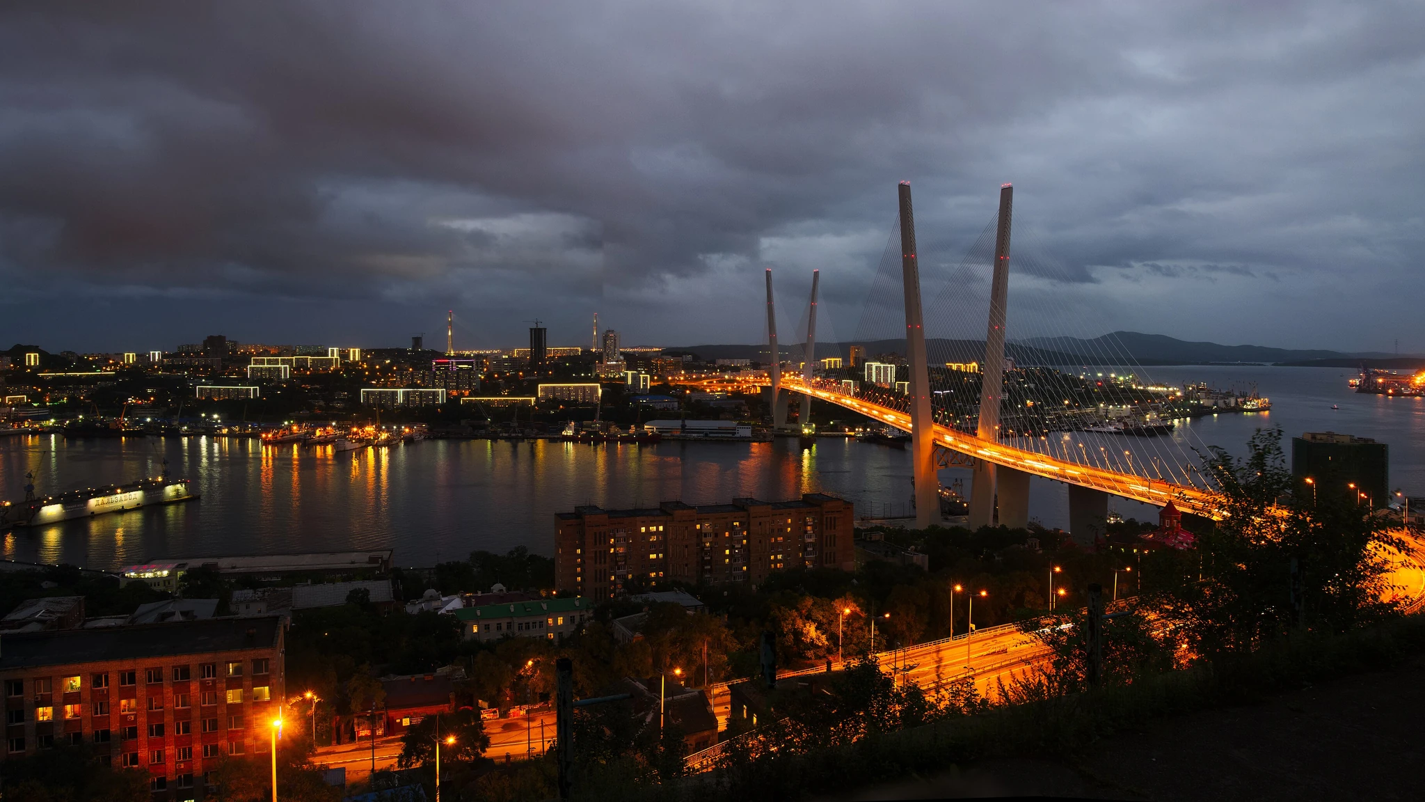 Освещённый вантовый мост над городской бухтой вечером