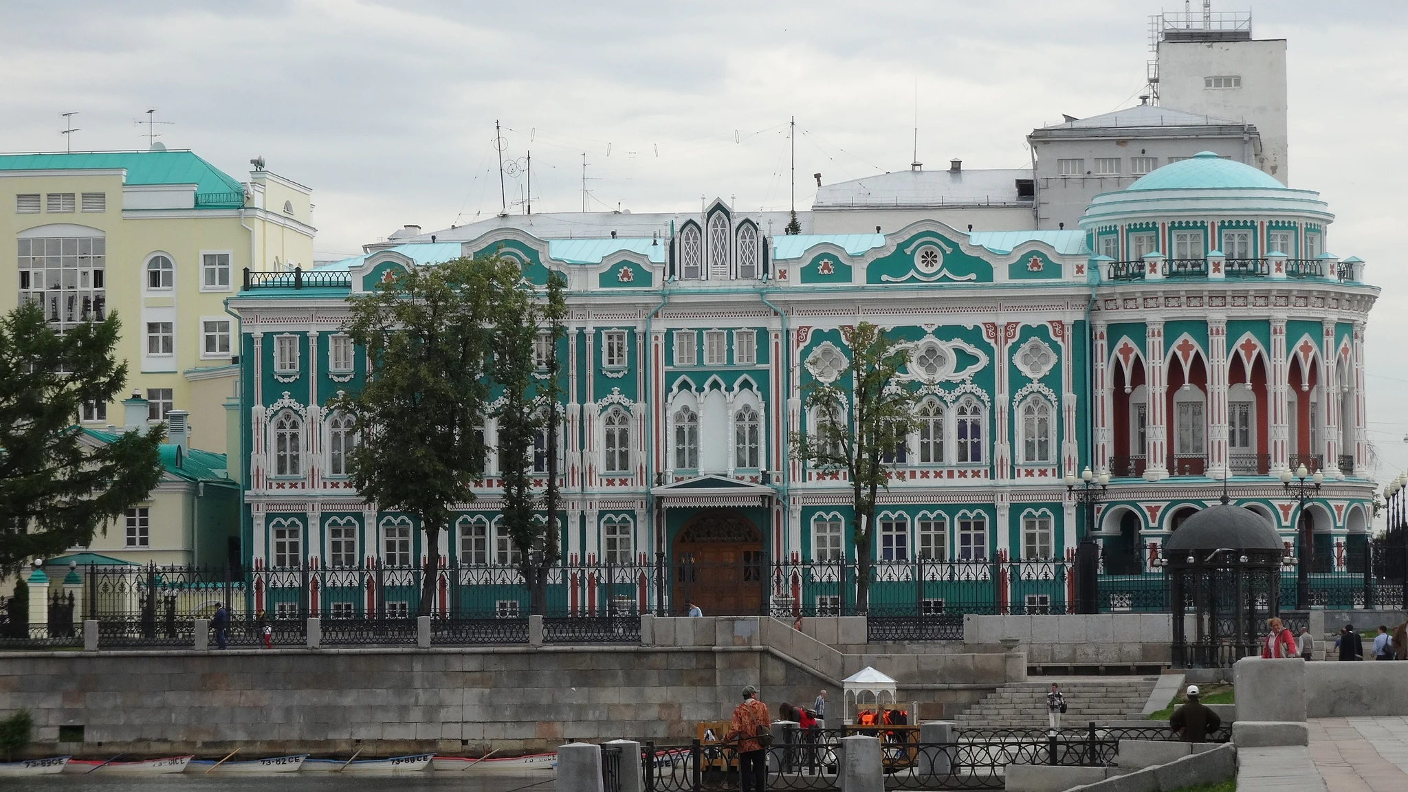 Бело-зелёный особняк с арочными окнами и красной крышей